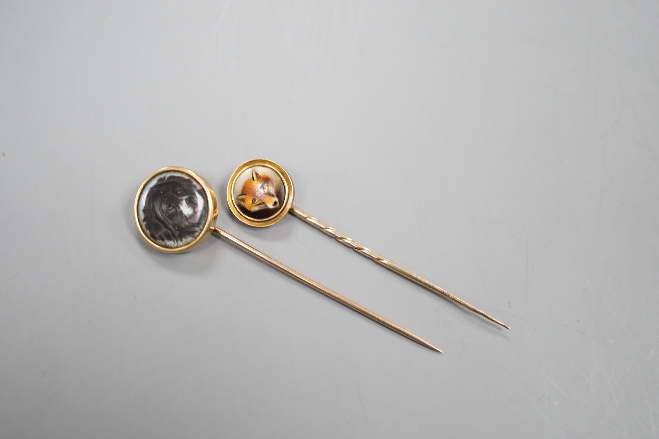 Two early 20th century yellow metal and enamel stick pins, both decorated with the head of a dog, largest, 70mm, gross weight 7.6 grams.